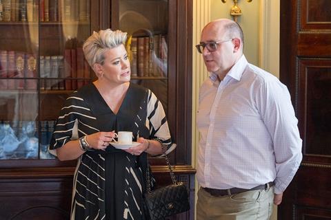 Two delegates stand next to each other, looking deep in conversation, over a cup of coffee.